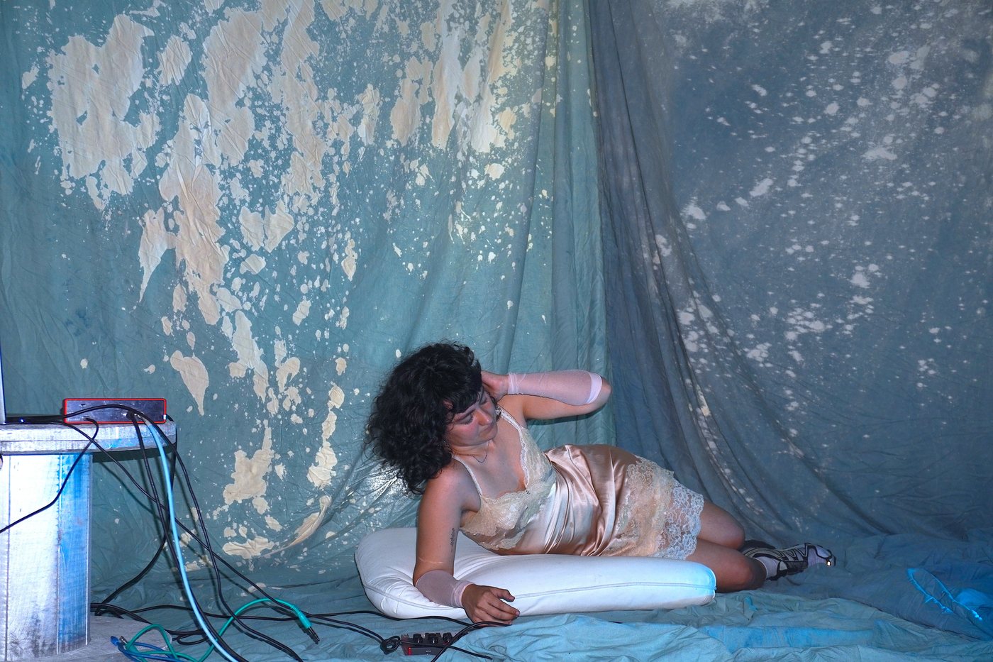 A performer lying on cushions in front of painted fabrics.