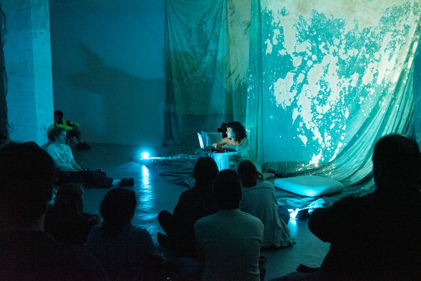The audience in front of hanging fabrics lit in turquoise.