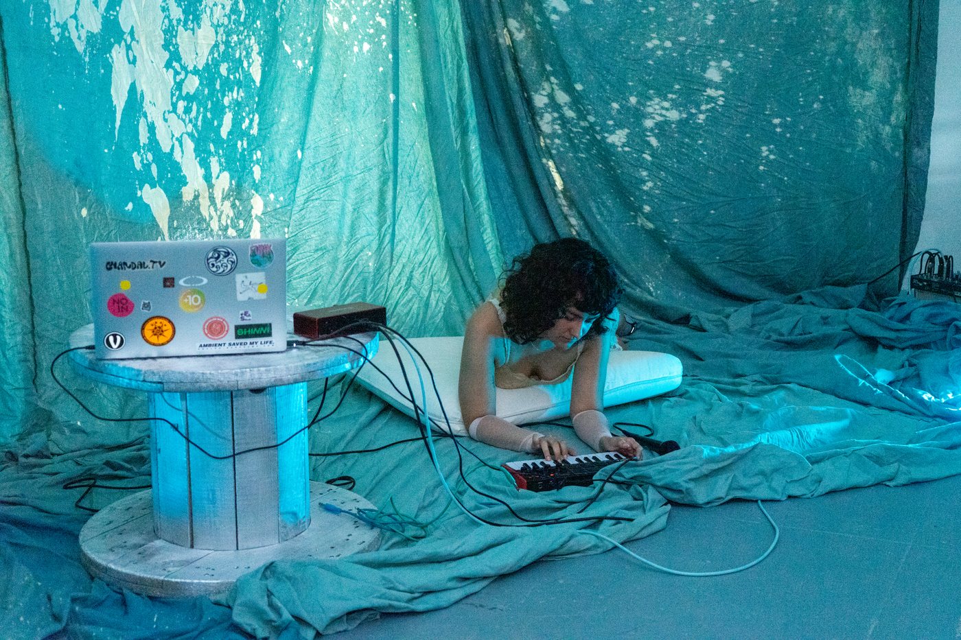 A performer at her sound setup on the floor, among turquoise fabrics.