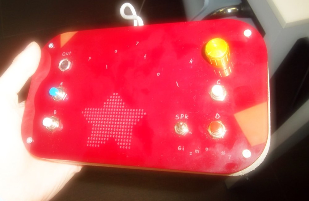 A red synthesiser with a star of holes, Playfolk Gizmo #7, held in a hand.